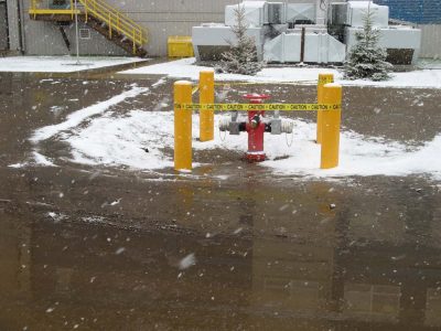 Fire hydrant protected by bollards and caution tape at an industrial plant